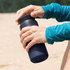 A drink bottle in navy blue, featuring a secure lid, held by a person wearing a teal long-sleeve top.