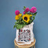 A tote bag in cream fabric displays a floral design and holds an assortment of vibrant flowers, including sunflowers and dahlias.