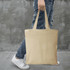 A beige tote bag carried by a person wearing jeans and white sneakers. The bag has handles and features a logo.