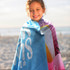 A young girl wrapped in a vibrant blue and pink beach towel with a playful design and a logo.