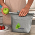 A grey cooler bag with a logo, held by a person, alongside a plate of strawberries and an apple.