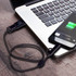 A braided charging cable in black, connected to a smartphone and a laptop on a wooden surface.
