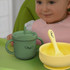 A drink bottle in green with a handle and straw, accompanied by a yellow bowl and spoon. The bottle features a logo.
