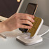 A wireless charging stand with a bamboo top and a white base, featuring a hand placing a phone on it.