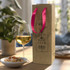 A champagne ribbon handle paper bag in natural brown with pink handles, beside a glass of white wine and snacks.