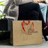 A brown paper bag with red ribbon handles, featuring a logo, rests on the ground beside a person sitting.