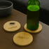 A green drink bottle rests on a round bamboo coaster, alongside two additional bamboo coasters with logos.