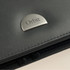 A grey document wallet featuring a metallic logo. The surface has a textured finish with visible stitching.