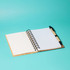 A bamboo notebook with a pen, featuring lined pages and a spiral binding, on a vibrant turquoise background.