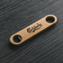 A bamboo bottle opener in a natural wood colour, featuring a logo and two openings.