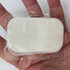 A hand holding a clear packaging containing a white, oval-shaped product. The product has a soft texture.