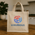 A beige jute tote bag with handles and a colourful logo printed on the front.