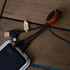 A bamboo charging cable with RPET connectors, featuring black fabric sheathing and an orange accent, on a wooden surface.
