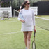 A drink bottle in a light blue colour, held by a person on a tennis court, wearing a white outfit and sunglasses.