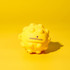 A yellow stress ball with a textured, spiky surface, featuring a small logo on it.