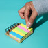 A mini bamboo sticky note set featuring vibrant pink, green, and yellow notes on a wooden base with a hand reaching for a note.