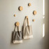 Two recycled cotton twill tote bags in grey and beige hanging on wooden pegs against a light wall.