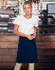 A woman wearing a navy canvas short waist apron over a white t-shirt, standing in a café setting.