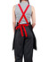 A black canvas bib apron with red straps worn over striped pants, featuring a tied waist and a logo on the back.