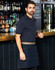 A man wearing a denim half apron stands at a bar, featuring a logo on the apron and a dark background with shelves of drinks.