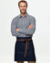 A man in a checkered shirt wears a denim half apron with a brown tie belt. The apron features pockets and a logo.