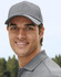 A grey cap features a structured design and a logo, worn by a smiling man in a casual setting.