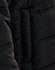 A close-up of a black heavy quilted jacket, highlighting the texture and stitching. The jacket features a brand logo.