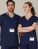 A navy scrub top with contrasting teal collar details, worn by a male and female model. Features pockets and identification badges.