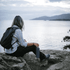 A drink bottle in grey sits beside a person on a rock, overlooking a tranquil body of water and distant mountains.