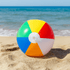 A brightly coloured beach ball with sections of red, yellow, green, and blue, resting on sand by the ocean.
