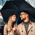 A black umbrella with blue accents is held above a couple smiling at each other in a city setting.