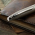 A sleek grey ballpoint pen rests on a leather notebook, featuring a logo on its side.