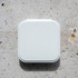 A white compact mirror with an LED light, featuring a square shape and a smooth surface, resting on a textured stone background.