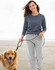 A woman walks a golden retriever on the beach, wearing a dark grey long-sleeve tee and grey sweatpants.