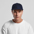 A wool cap in navy blue, featuring a solid design and a logo, worn by a model in a white shirt.