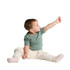 A seated infant wearing a green organic t-shirt and light-coloured trousers, reaching out with one hand.