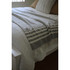 A throw blanket in grey and white striped pattern drapes over a white bedspread with pillows in the background.