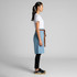 A denim half apron in light blue, featuring a brown tie at the waist, displayed on a model in profile.