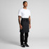 A man wearing a black linen half apron over a white t-shirt and black pants, standing confidently.