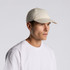 A light-coloured cap worn by a man with a neutral expression, featuring a logo on the front.
