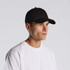 A black cap is worn by a model, featuring a simple design and a logo on the front.