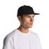 A black cap with a flat brim, featuring a logo on the front, displayed on a model wearing a white shirt.