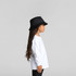 A child in a white long-sleeve tee and a black bucket hat, standing in profile against a neutral background.