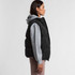 A puffer vest in black, featuring a hood and worn over a grey sweatshirt, displayed from the side.