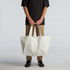 An oversized tote bag in off-white held by a person, featuring strong handles and a simple design.