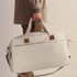 A duffle bag in light grey, being carried by a person with a neutral outfit, featuring a logo and leather accents.