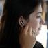 A woman is wearing black Prixton TWS157 earbuds in her ear, adjusting one while looking off to the side.