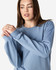 A blue Gildan Softstyle adult sweatshirt is worn by a model adjusting their sleeves, featuring a logo on the garment.