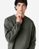 An olive green Gildan Softstyle adult sweatshirt displayed on a male model, featuring a simple design and crew neck.