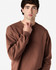 A brown Gildan Softstyle adult sweatshirt worn by a model, featuring a simple design and a logo.